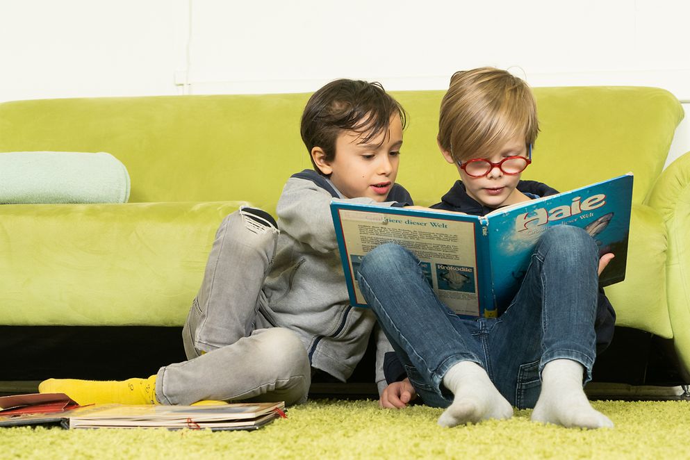 Das Bild zeigt zwei Kinder, die ein Buch lesen