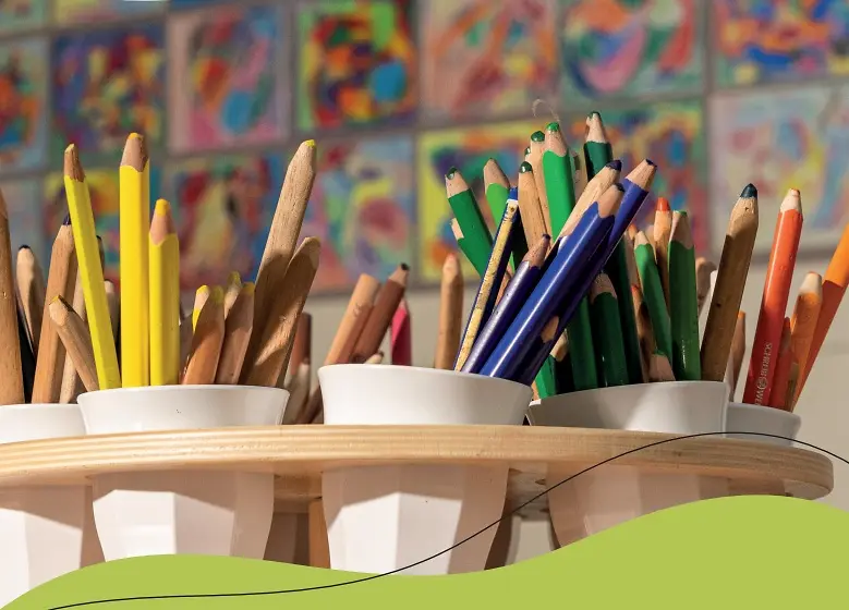 Viele Buntstifte stehen in Bechern auf einem Tisch.